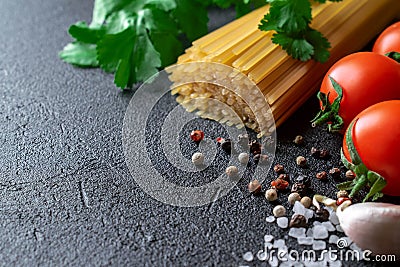 Raw spaghetti on a black background with tomatoes, spices and coarse sea salt Stock Photo