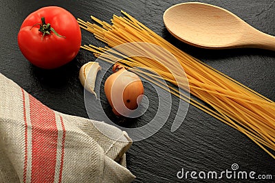 Raw spaghetti with tomato, garlic, onion, wooden trowel and kitchen towel Stock Photo