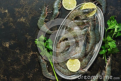 Raw tiger prawns on a metal plate with ice, lemon and parsley on a dark background. Top view, copy space Stock Photo