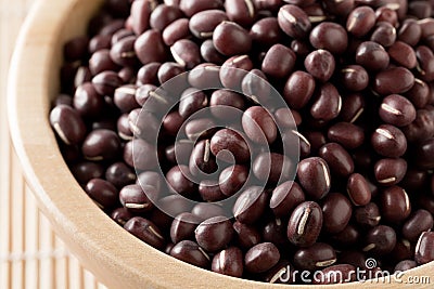 Raw, uncooked, dried adzuki red mung beans in wooden bowl on bamboo mat background Stock Photo