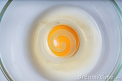 Raw uncooked egg in bowl. Yolk in center. Flat view from above. Stock Photo