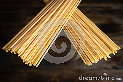 Raw uncooked Italian spaghetti , two stacks of pasta crossed over a dark wooden background Stock Photo
