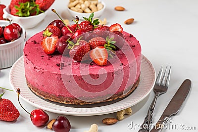 Raw vegan berry cheesecake with fresh strawberries and cherries on white background with fork and knife. close up Stock Photo