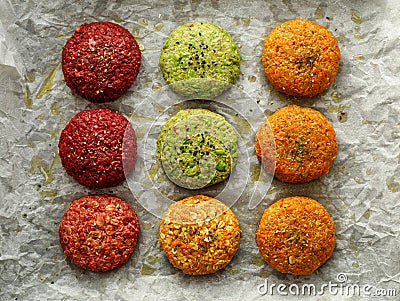 Raw vegan burgers made of beetroot, green peas, carrots, groats and herbs on white parchment prepared for baking, top view. Stock Photo