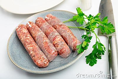 Raw white botifarra sausages on plate with knife and fresh parsley Stock Photo