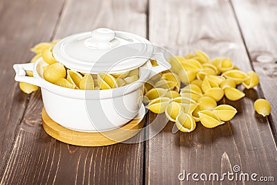 Raw yellow pasta conchiglie on brown wood Stock Photo