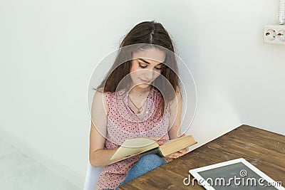 Reading, education, culture, people concept - young student woman is reading a book, while she is sitting on white chair Stock Photo