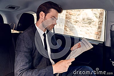 Reading latest news. Handsome young man in full suit reading a newspaper while sitting in the car Stock Photo