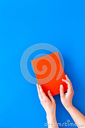 Reading for leasure. Hands take hardback book with empty cover on blue background top view space for text Stock Photo
