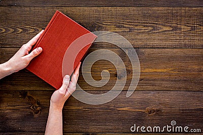 Reading for leasure. Hands take hardback book with empty cover on dark wooden background top view space for text Stock Photo