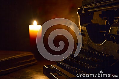 Reading and writing scenes in ancient times: an old book and an old typewriter on a ruined wooden table lit by a candle on a woode Stock Photo