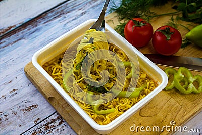 Ready noodles in cup with vegetables and herbs on a wooden board. Stock Photo