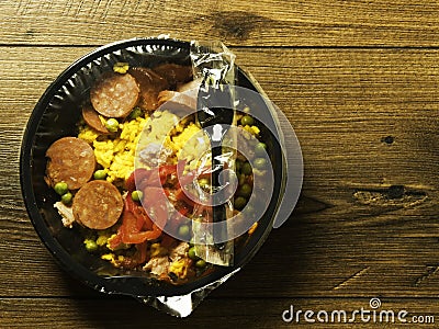 Ready made Spanish paella in a black plastic dish for microwave on a wooden table. Premium quality meal for take away or on the go Stock Photo