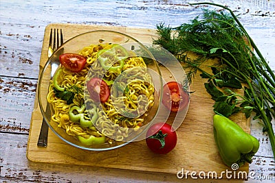 Ready noodles in cup with vegetables and herbs on a wooden board. Stock Photo