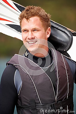 Ready to get out on the waves. Smiling water-skier holding his skis alongside the lake. Stock Photo