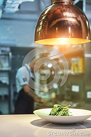 Ready to serve. Vertical photo of fresh green salad standing on the table under the light with working chef on the Stock Photo