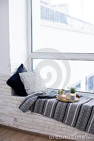 Real apartment interior decor, aromatic candles and plants on vintage tray with pillows and blanket on white windowsill Stock Photo