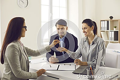 Real estate agent gives the keys to her new home to a married couple at a meeting in the office. Stock Photo