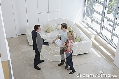 Real Estate Agent Shaking Hands With Man By Woman In New Home Stock Photo