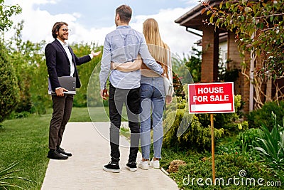 Real estate broker showing house for sale to young couple, outside Stock Photo