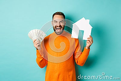 Real estate concept and mortgage concept. Ecstatic caucasian man holding money dollars and house maket, shouting for joy Stock Photo