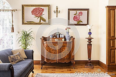 Real photo of an antique cabinet with porcelain decorations, paintings with roses and blue sofa in a living room interior Stock Photo