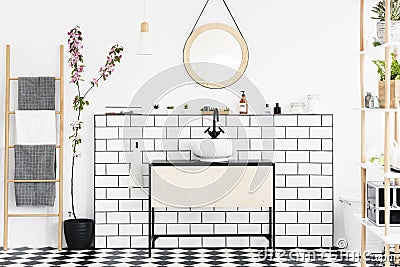 Real photo of a bathroom interior with a cupboard, tiles, mirror, flower and ladder with towels Stock Photo