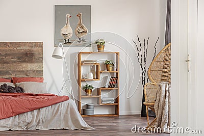 Real photo of a bedroom interior with an oil painting, wooden bookcase and a bed with red and white sheets Stock Photo