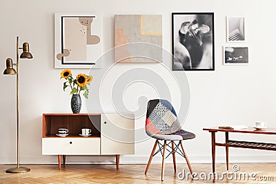 Real photo of bright eclectic living room interior with many posters, colorful chair, wooden cupboard with flowers and coffee tabl Stock Photo