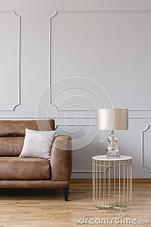 Real photo of bright living room interior with leather couch with pillow, end table with glass lamp Stock Photo