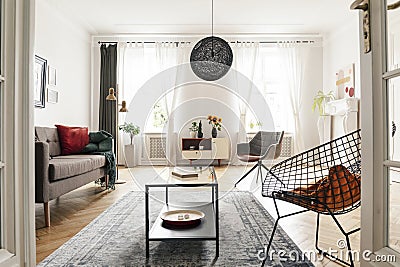 Bright living room interior with a metal armchair, coffee table and sofa. Big lamp in the middle. View through a d Stock Photo