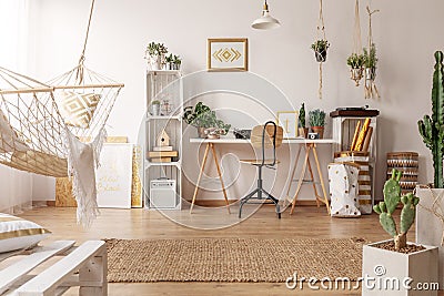 Bright room interior with hammock, fresh plants and home office corner with wooden desk, chair and decor Stock Photo