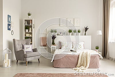 Real photo of a feminine bedroom interior with a comfy armchair, bed, plants and shelf Stock Photo