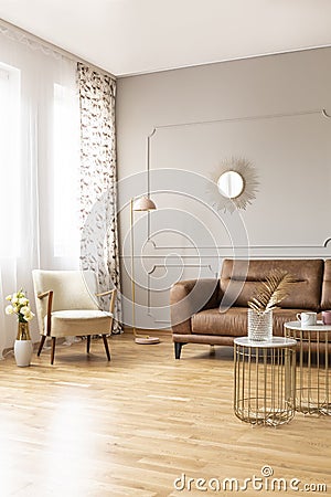 Real photo of full of light daily room with retro armchair, lamp, brown leather couch and tables Stock Photo