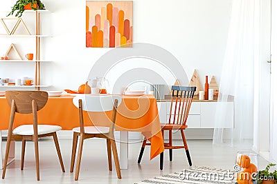 Kitchen table covered with orange tablecloth and white dishes. Artwork on the wall and shelf in the corner Stock Photo