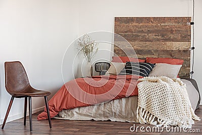 Real photo of a leather chair in a natural bedroom interior with a wooden bed, white walls and string of lights Stock Photo