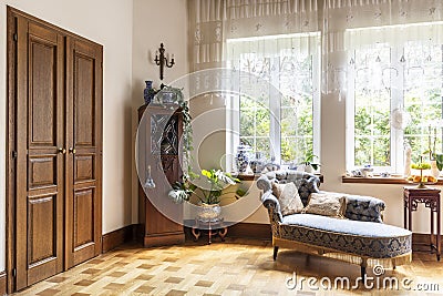 Real photo of a living room interior with a chaise longue, porcelain vases, wooden door and windows with curtains Stock Photo