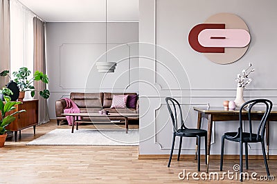 Real photo of open space living room interior with modern clock on wall with molding, table with black chairs and leather sofa in Stock Photo