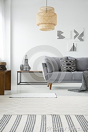 Real photo of a rattan lamp hanging above a gray settee with a b Stock Photo