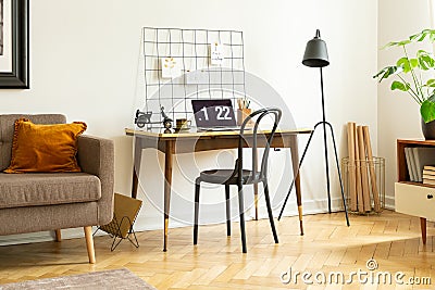 Real photo of a simple desk with a laptop, chair, wall organizer next a sofa in a home office interior Stock Photo