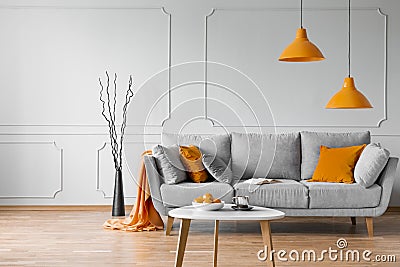 Real photo of simple living room interior with orange lamps, pillows and grey sofa Stock Photo