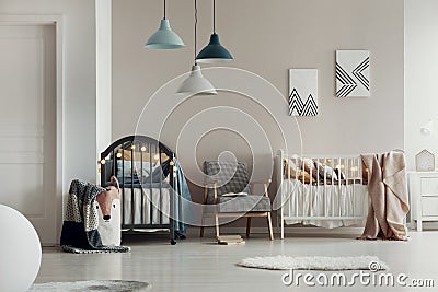 Real photo of a spacious, white and beige bedroom interior for twins with two wooden cribs and an armchair Stock Photo