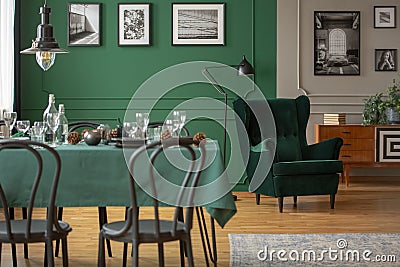 Real photo of a table with green cloth and black chairs in blurred foreground and a comfy armchair in the background in dining Stock Photo