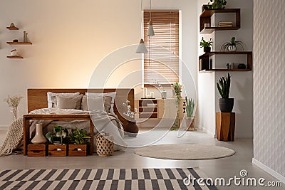 Real photo of a warm bedroom interior with wooden boxes and shelves, double bed and plant. Empty wall, place your logo Stock Photo