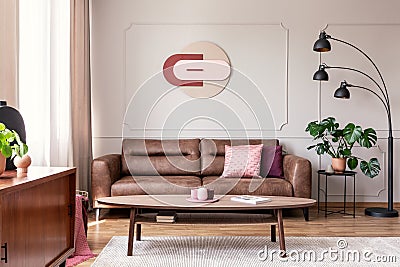 Real photo of wooden coffee table placed on carpet in bright sitting room interior with leather brown couch, modern clock on wall, Stock Photo