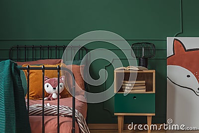 Photo of a wooden nightstand standing against green wall, between a fox painting and a bed for a kid in a cute interior Stock Photo