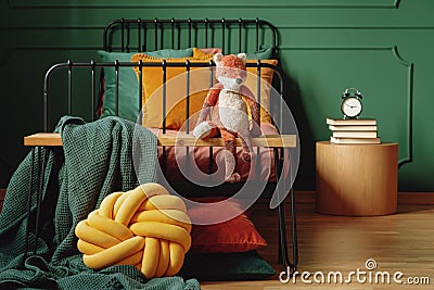 Real photo of a knot pillow, green blanket and plush fox on a wooden bench in front of a black bed in cute bedroom interior Stock Photo