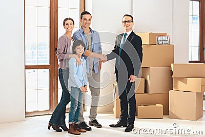 Realtor with family in new apartment with cardboard boxes. Father and realtor are shaking hands. Stock Photo