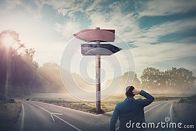 Rear businessman in front of crossroad and signpost arrows shows two different courses, left and right direction to choose. Road Stock Photo