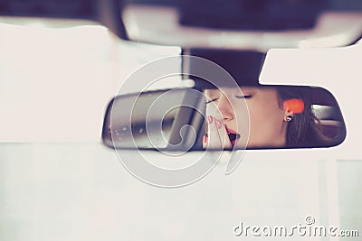 Rear mirror view of a sleepy yawning woman driving her car after long hour drive. Stock Photo